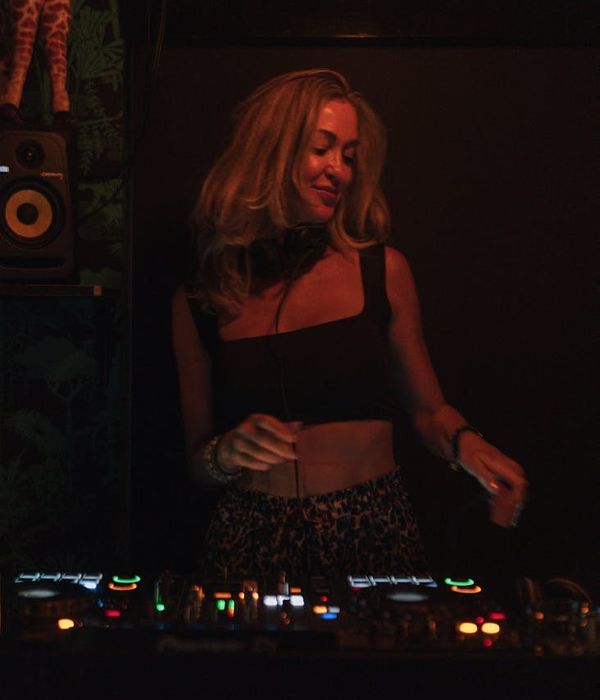 Woman performing a light, energetic stretch in a modern, dark room.